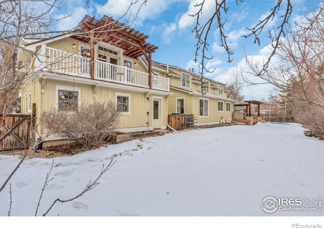 snow covered rear of property with a balcony and a pergola