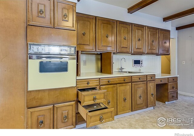 kitchen featuring tasteful backsplash, beam ceiling, oven, and sink