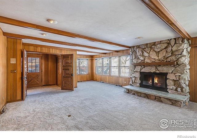 unfurnished living room with light carpet, a textured ceiling, wooden walls, beamed ceiling, and a fireplace