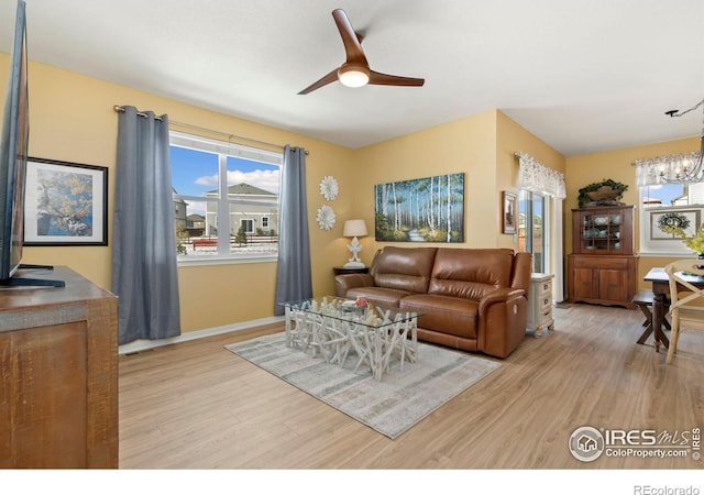 living room with ceiling fan with notable chandelier and light hardwood / wood-style floors