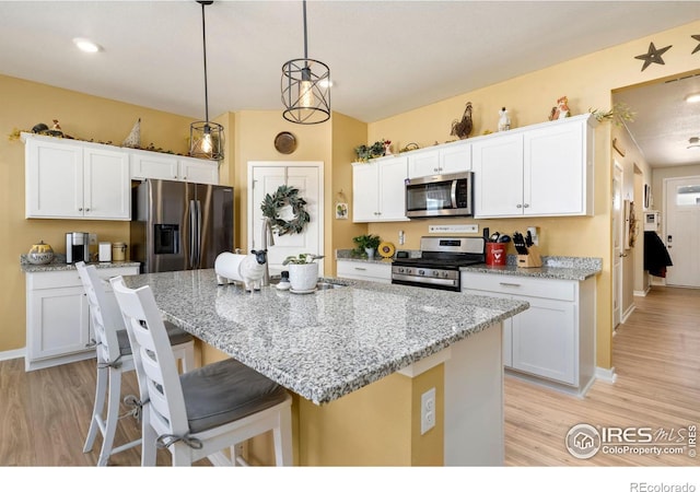 kitchen with appliances with stainless steel finishes, a kitchen island with sink, white cabinets, and a kitchen bar