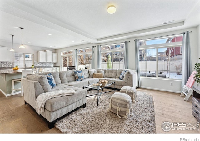 living room with sink, beam ceiling, a textured ceiling, and light wood-type flooring