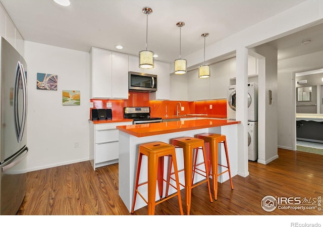 kitchen featuring appliances with stainless steel finishes, tasteful backsplash, white cabinetry, stacked washer and clothes dryer, and a center island