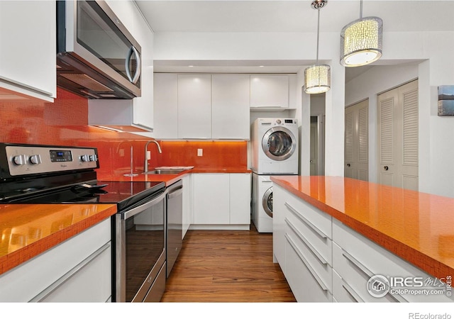 kitchen with sink, hanging light fixtures, appliances with stainless steel finishes, stacked washing maching and dryer, and white cabinets