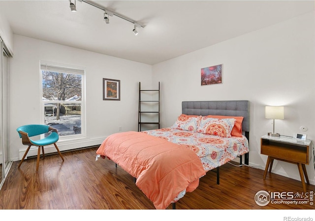 bedroom with a baseboard heating unit, hardwood / wood-style flooring, and rail lighting