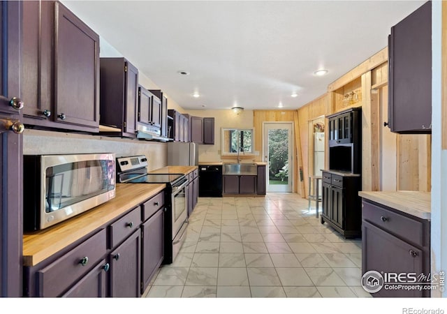 kitchen with dark brown cabinetry, sink, wooden counters, appliances with stainless steel finishes, and wooden walls