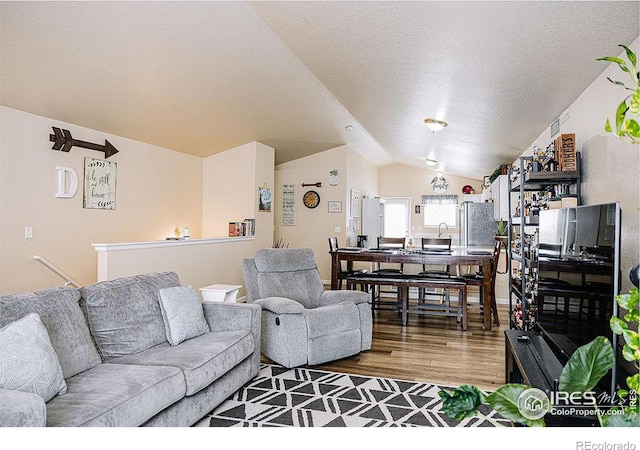 living room with wood-type flooring, vaulted ceiling, and a textured ceiling