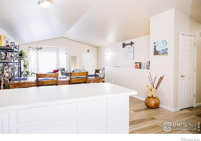 kitchen featuring vaulted ceiling, white cabinets, and light wood-type flooring