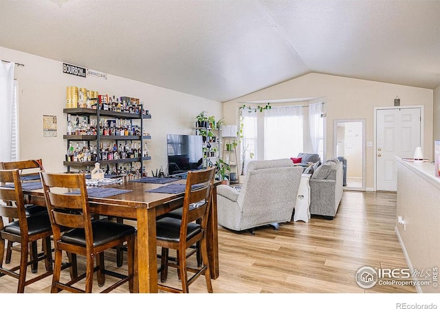 dining area with vaulted ceiling, light hardwood / wood-style flooring, and a textured ceiling