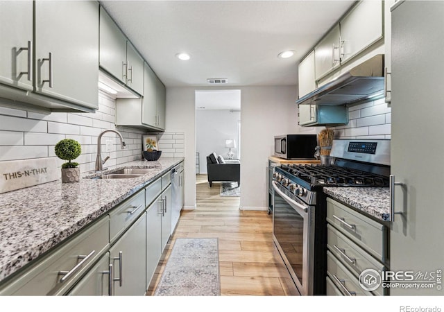 kitchen with sink, light hardwood / wood-style flooring, backsplash, stainless steel appliances, and light stone counters