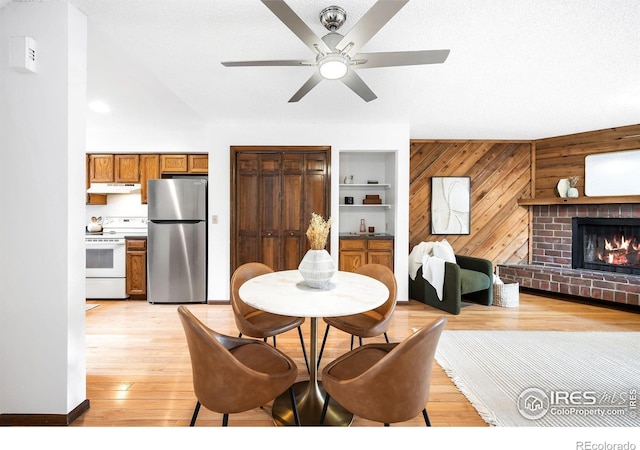 dining area with light hardwood / wood-style flooring, ceiling fan, wooden walls, a fireplace, and a textured ceiling