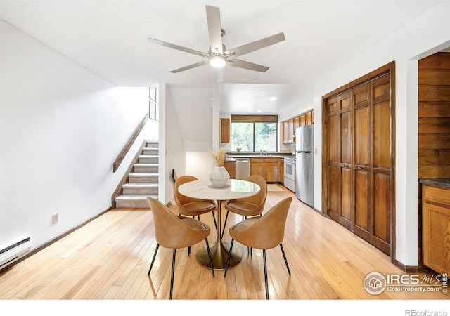 dining area with a baseboard heating unit, a textured ceiling, and light hardwood / wood-style flooring