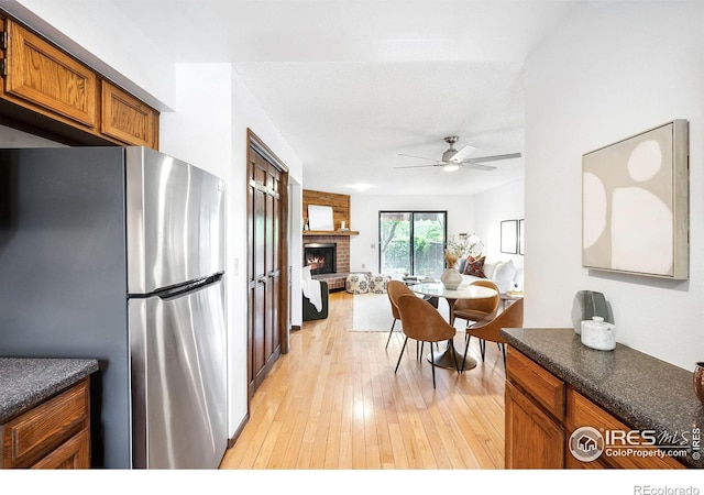 kitchen featuring ceiling fan, stainless steel fridge, light hardwood / wood-style floors, and a fireplace