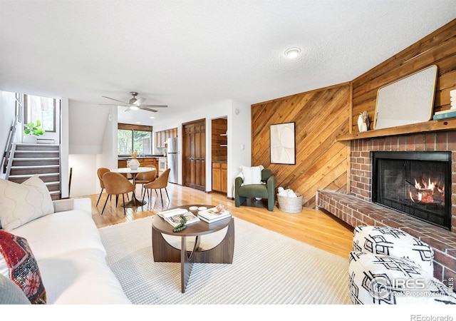 living room with wood-type flooring, wooden walls, a brick fireplace, and a textured ceiling