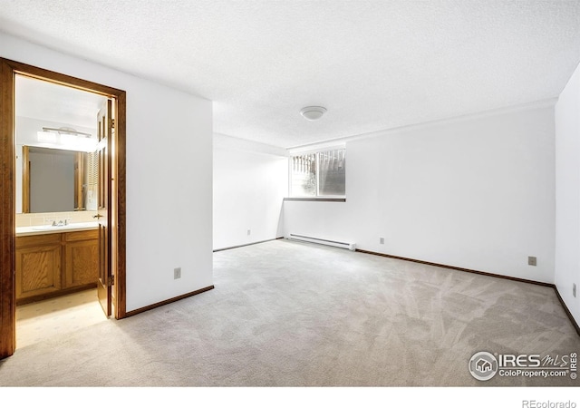 carpeted spare room featuring baseboard heating, sink, and a textured ceiling