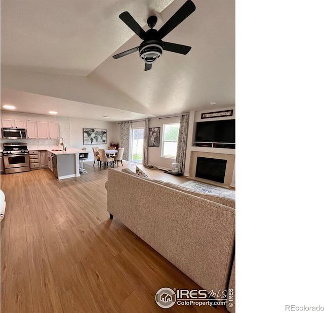 living room featuring lofted ceiling, sink, ceiling fan, and light hardwood / wood-style flooring