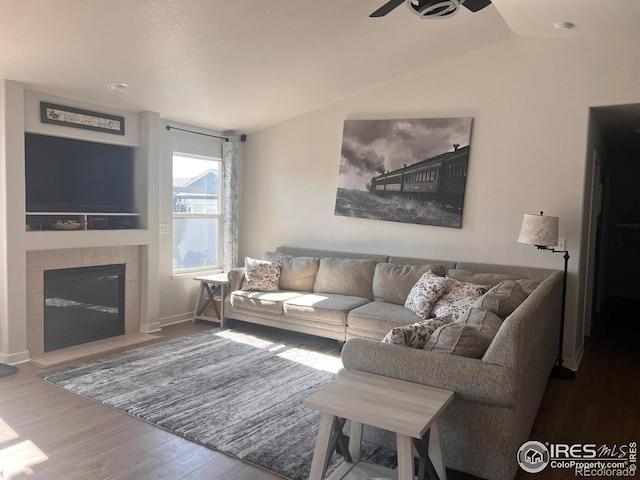 living room featuring vaulted ceiling, ceiling fan, a tiled fireplace, and hardwood / wood-style floors