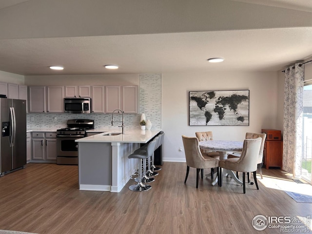 kitchen featuring sink, appliances with stainless steel finishes, gray cabinetry, a kitchen breakfast bar, and kitchen peninsula