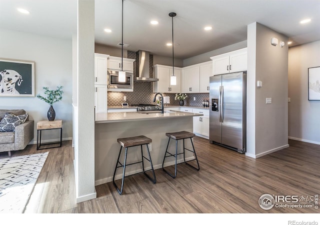 kitchen featuring appliances with stainless steel finishes, white cabinetry, a kitchen breakfast bar, hanging light fixtures, and wall chimney exhaust hood