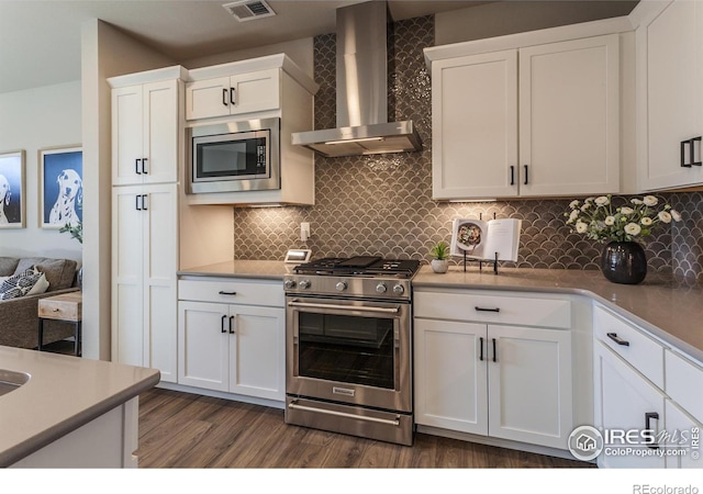 kitchen featuring appliances with stainless steel finishes, dark hardwood / wood-style floors, white cabinets, backsplash, and wall chimney exhaust hood