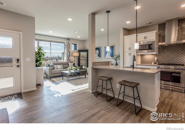 kitchen featuring a kitchen bar, wall chimney range hood, kitchen peninsula, stainless steel appliances, and white cabinets