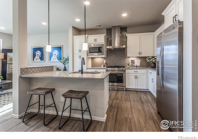 kitchen with wall chimney exhaust hood, sink, white cabinetry, pendant lighting, and stainless steel appliances