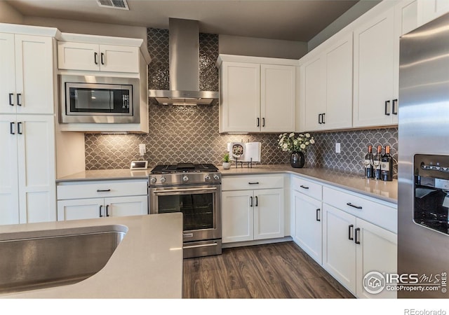 kitchen featuring backsplash, white cabinets, dark hardwood / wood-style flooring, stainless steel appliances, and wall chimney range hood