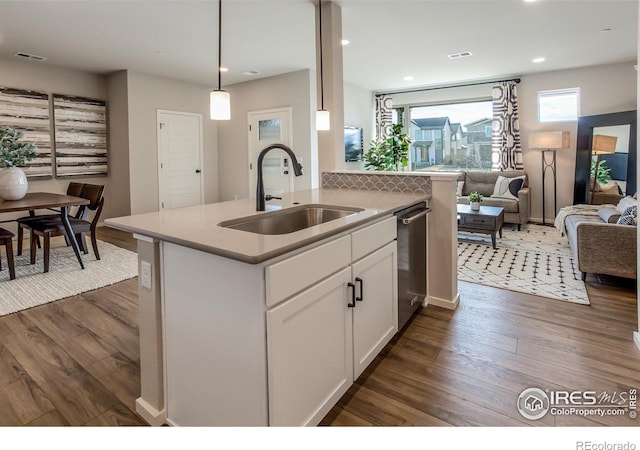 kitchen featuring sink, white cabinetry, decorative light fixtures, dark hardwood / wood-style flooring, and an island with sink