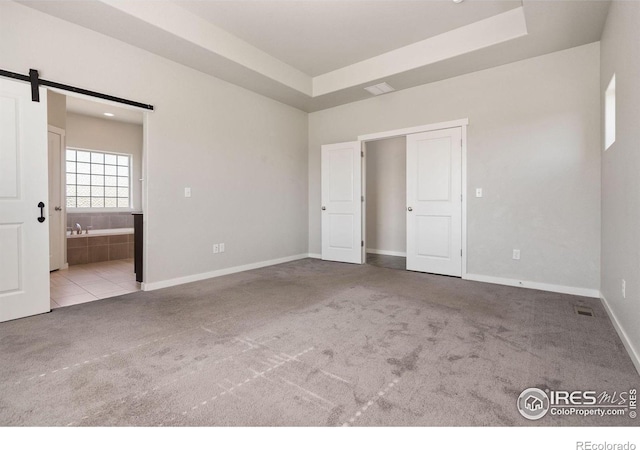 unfurnished bedroom with light carpet, connected bathroom, a raised ceiling, and a barn door