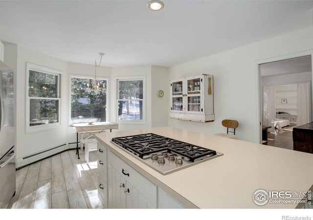 kitchen featuring stainless steel gas cooktop, hanging light fixtures, light wood-type flooring, a baseboard radiator, and white cabinets