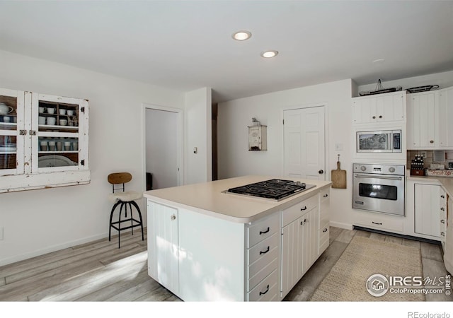 kitchen featuring a kitchen island, white cabinetry, backsplash, stainless steel appliances, and light hardwood / wood-style flooring