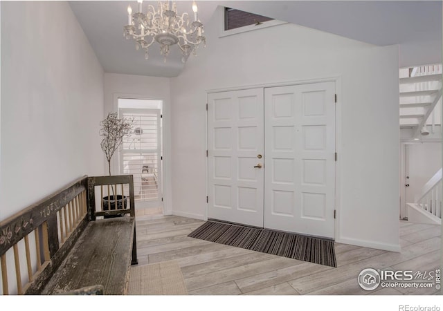 foyer entrance featuring lofted ceiling, an inviting chandelier, and light hardwood / wood-style flooring