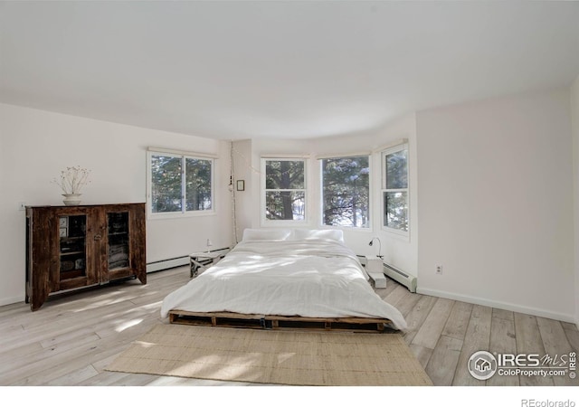 bedroom featuring multiple windows, a baseboard heating unit, and light wood-type flooring