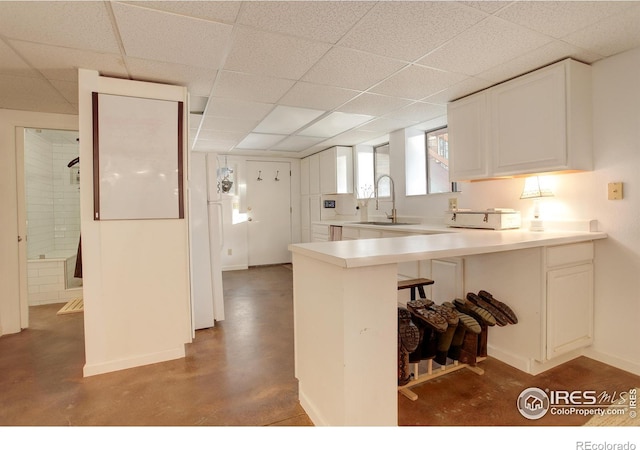 kitchen featuring concrete flooring, sink, a breakfast bar area, white cabinets, and kitchen peninsula