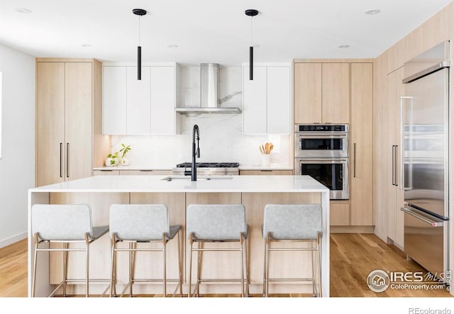 kitchen featuring hanging light fixtures, wall chimney exhaust hood, white cabinets, and appliances with stainless steel finishes