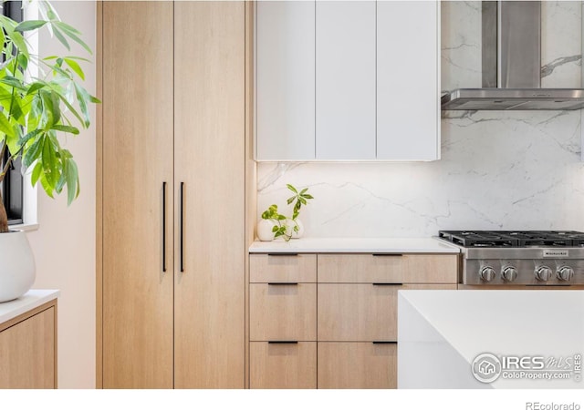 kitchen with light brown cabinetry, wall chimney range hood, backsplash, and stainless steel gas stovetop