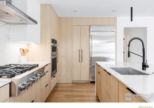 kitchen featuring wall chimney exhaust hood, stainless steel appliances, sink, and light brown cabinets