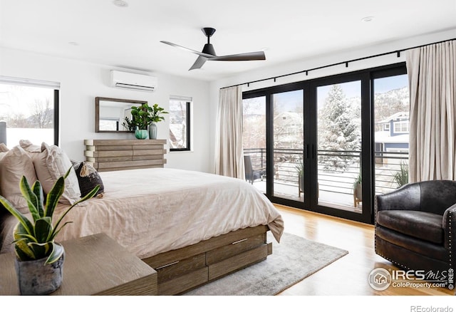 bedroom with ceiling fan, access to outside, a wall mounted AC, and light wood-type flooring