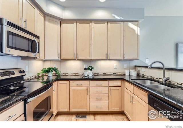 kitchen featuring sink, dark stone countertops, stainless steel appliances, light hardwood / wood-style floors, and decorative backsplash