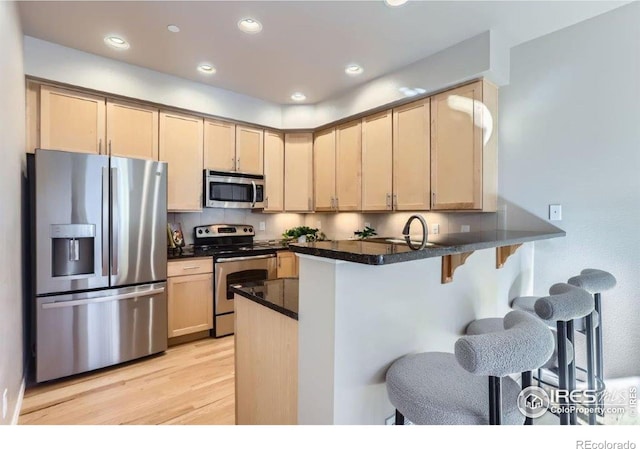 kitchen featuring light hardwood / wood-style flooring, light brown cabinets, a kitchen breakfast bar, kitchen peninsula, and stainless steel appliances