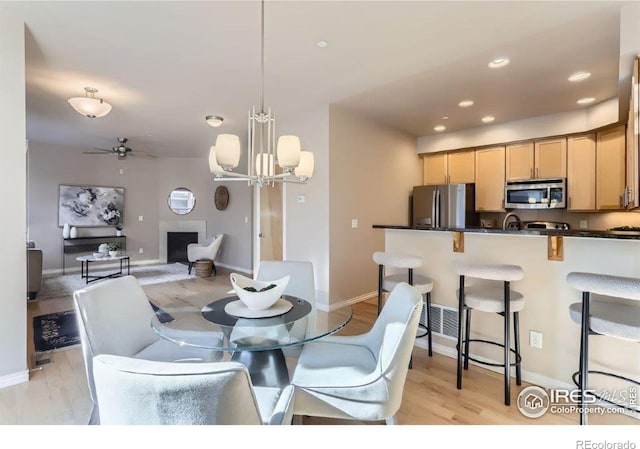 dining space with ceiling fan with notable chandelier and light hardwood / wood-style floors