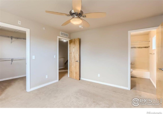 unfurnished bedroom featuring connected bathroom, a spacious closet, light carpet, a closet, and ceiling fan