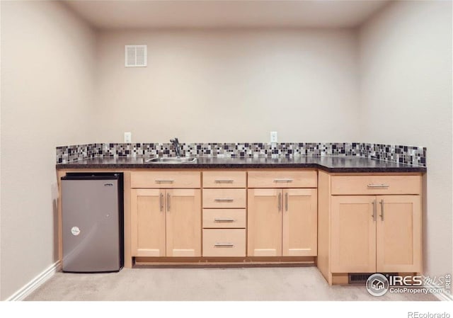 kitchen featuring stainless steel refrigerator, light brown cabinetry, sink, and backsplash