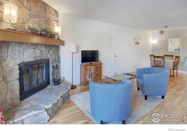 living room with a stone fireplace, a textured ceiling, and light wood-type flooring