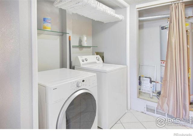 clothes washing area with gas water heater, separate washer and dryer, and light tile patterned floors