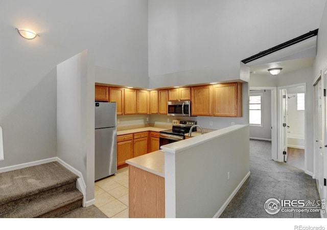 kitchen with appliances with stainless steel finishes, sink, a high ceiling, light tile patterned floors, and kitchen peninsula