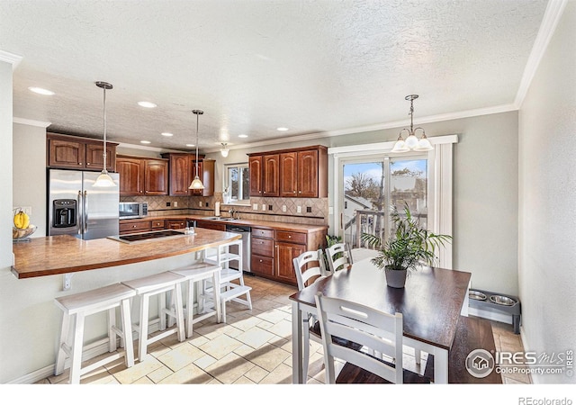 kitchen with appliances with stainless steel finishes, pendant lighting, a kitchen breakfast bar, decorative backsplash, and a textured ceiling