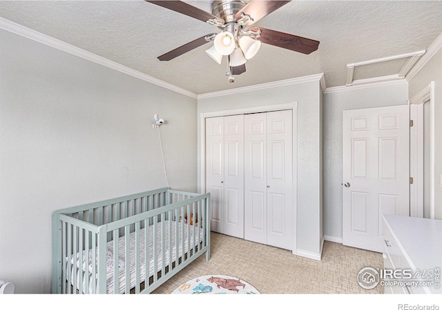 bedroom featuring ceiling fan, a crib, crown molding, a textured ceiling, and a closet