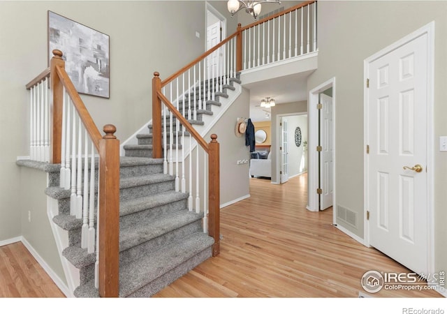 staircase with an inviting chandelier, hardwood / wood-style floors, and a high ceiling