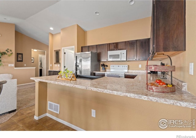 kitchen featuring white appliances, dark brown cabinetry, light stone counters, vaulted ceiling, and kitchen peninsula